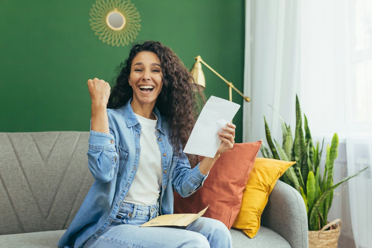 portrait-of-happy-woman-at-home-hispanic-woman-smiling-and-looking-at-camera-holding-envelope-with.jpg
